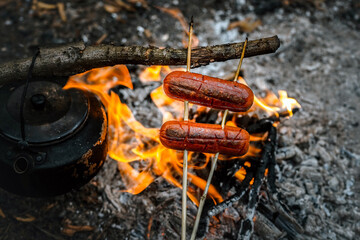 campfire sausage in pan, water bottle and titanium mug near the fire outdoors. bushcraft, adventure,