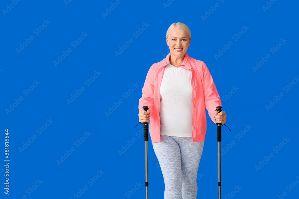 Mature woman with walking poles on color background