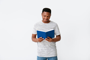 Wall Mural - African-American man reading book on light background