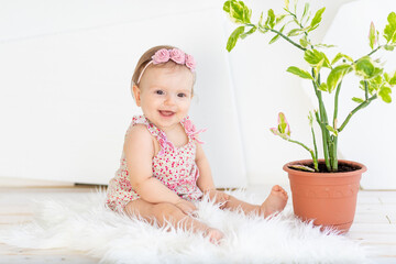 smiling little child girl sitting in a bright white room in a red dress with a room flower