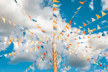 Colorful Bright Triangular Bunting Flags On A Blue Sky Background With White Clouds. Concept Of Celebration And Fun.