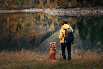 Traveling with the dog. A girl and a dog stand by a mountain lake in autumn. 