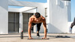 Shirtless muscular male athlete doing high plank leg lift exercise in the open air on building rooftop