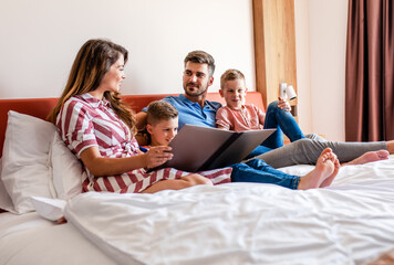 Wall Mural - family of four enjoying together at hotel room, sitting at bed reading hotels offers.