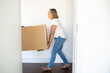 © Mangostar - Woman moving into apartment, carrying cartoon box. Side view from doorway. Relocation concept