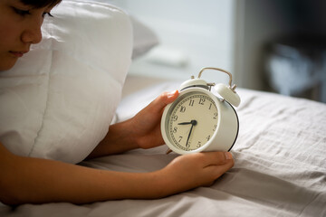 a schoolboy holding the white vintage alarm clock to set the alarm for the day after, the clock showing time at 8 o'clock (8 pm) in the evening. Bed time for kids.