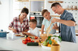 © JustLife - Mother and father making breakfast with sons. Young family preparing delicious food in kitchen..