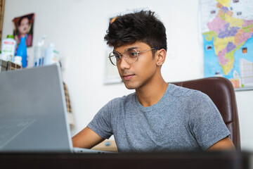 Indian teenager working on his laptop while looking into the camera.