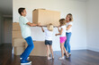 Focused parents and two girls carrying boxes into new empty flat together. Full length. Real estate purchase concept