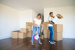 Joyful parents and kids enjoying new home, dancing and having fun near heaps of boxes in empty room. Full length. Apartment buying concept
