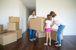 Happy parents and girl carrying box into new empty flat together. Full length. Real estate purchase concept