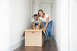 Happy Caucasian parents playing with children sitting in carton box at new home. Joyful family enjoying new house. Mom, dad and daughters having fun during removal. Relocation and moving day concept