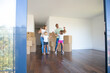 Cheerful parents and daughters dancing and having fun near heaps of boxes while moving into new flat. Full length, wide shot. Apartment buying or new home concept