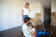 Cheerful parents and two daughters enjoying their new home. Girls hugging dad sitting on floor in empty room with boxes. Apartment buying concept