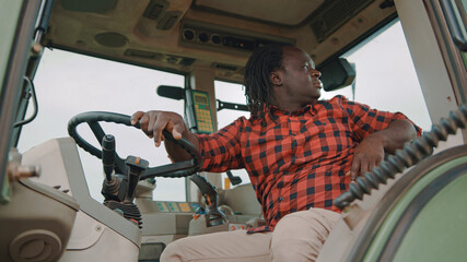 Young african farmer sitting in the tractor cabine and looking through the back window. High quality photo