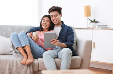 Wall Mural - Asian Couple Using Digital Tablet Sitting On Sofa At Home