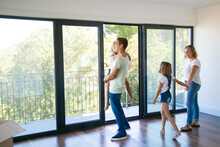 Happy Father With Daughter Standing Near Open Balcony And Smiling. Blonde Mother Holding Girl Hand And Talking With Her. Enjoying Family Watching New House Or Flat. Relocation And Mortgage Concept