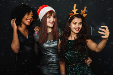 Wall Mural - A group of female friends of different nationalities take a Christmas selfie in the studio. Young women in santa hats and deer antlers are having fun together