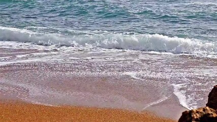 Wall Mural - Waves of light blue water at a sandy beach in Greece. Ripples are travelling faster to approach a beach. Beautiful footage of wavy water medium on a sunny day. Close uo