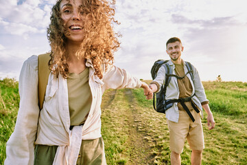 Canvas Print - Cheerful young couple with bags holding hands and moving along country road while hiking together in autumn