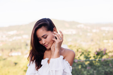 Outdoor portrait of asian woman in dress wearing necklace, earings and ring.