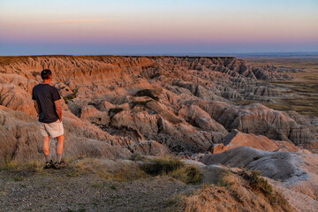 Person, man, standing on the edge of the cliff watching the canyon wall of dropping rock ridges from a high plateau to the valley below, Badlands National Park, South Dakota