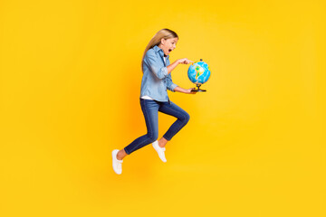 Wall Mural - Full length body size photo of amazed jumping high schoolgirl keeping globe pointing on continent shouting amazed isolated on bright yellow color background