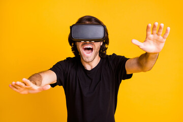 Photo of young man play virtual reality raise hands open mouth wear vr helmet t-shirt isolated yellow color background