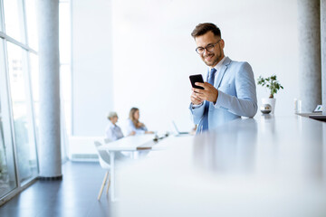 Happy young man using his mobile phone and smiling while his colleagues working in the background