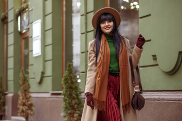 happy smiling woman wearing trendy autumn, winter beige coat, hat, brown scarf, gloves, pleated skir