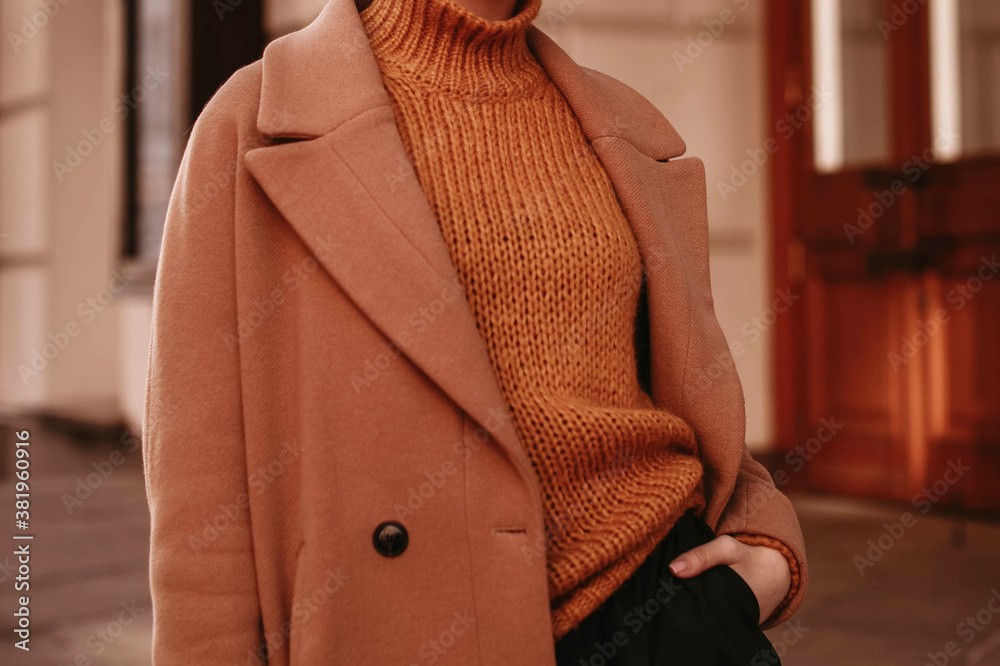 Young woman  with cropped head in the orange knitted cozy sweater and brown coat standing on the street. Outdoor portrait in daylight. Autumn colours.  - obrazy, fototapety, plakaty 