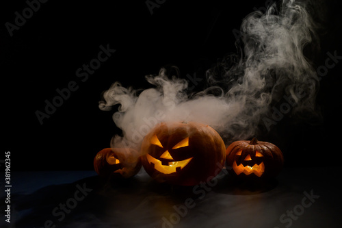 Cuadros en Lienzo Three creepy halloween steaming pumpkins with a carved luminous smirk on a black background