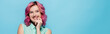 © LIGHTFIELD STUDIOS - young woman with pink hair smiling and flirting isolated on blue, panoramic shot