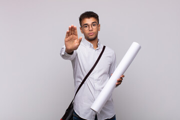 Wall Mural - young architect man looking serious, stern, displeased and angry showing open palm making stop gesture