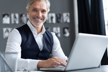 Canvas Print - Concentrated at work. Happy mature man in full suit using laptop while working in modern office