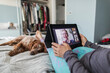 © Paul Bradbury/Caia Image - Woman with digital tablet video chatting with friends on bed with dog
