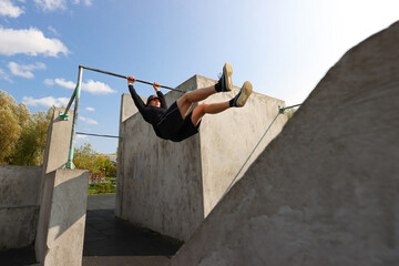 The guy is hanging on a horizontal bar on a sports field on the street