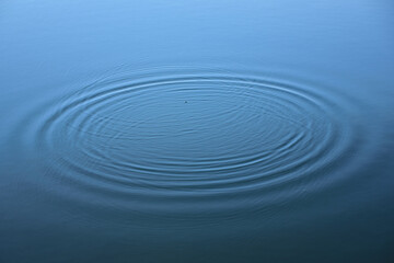 Background from the surface of a water, from which small ripples pull themselves in a circle from the inside out