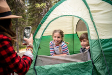 Mother With Smart Phone Photographing Kids In Tent At Campsite