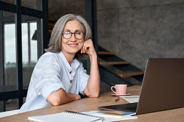Wall Mural - smiling stylish mature middle aged woman sits at desk with laptop, portrait. happy older senior busi