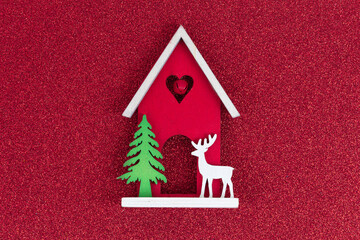 Christmas flatlay layout. wooden toy house, a deer and a Christmas tree on a red glitter shiny background. Christmas card with place for text