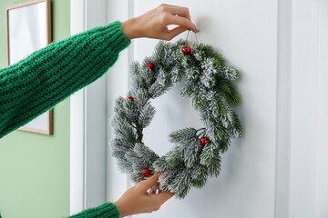 Woman hanging beautiful Christmas wreath on door