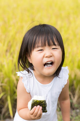 Wall Mural - 稲穂の実った秋の田んぼで美味しい新米おにぎりを食べる子供