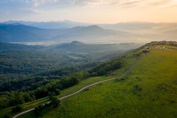 Early morning in the mountains. Morning sun and haze in the valley against the background of mountains. Green fields and meadows. The road leaving into the distance.