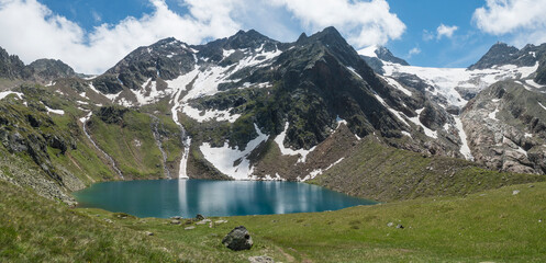 Panoramic view of turquoise blue mountain lake Grunausee in alpine landscape with green meadow and snow-capped mountain peaks. Tyrol, Stubai Alps, Austria, summer sunny day