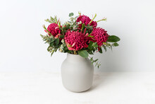 A Bunch Of Australian Native Red Waratah Flowers And Eucalyptus Leaves, In A Stylish Ceramic Grey Vase On A Table, With A White Background.