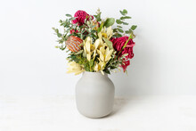 Elegant Flower Arrangement Of Australian Native Red Waratah Flowers, Orange Banksia, Yellow Leucadendrons And Eucalyptus Leaves, In A Grey Vase On A Table. Could Be A Gift On Display Or Decoration.