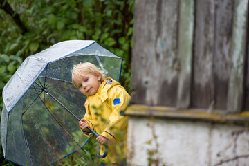 Poster - Cute blond toddler child, boy, playing in the rain with umbrella on a foggy autumn day