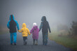 Four children, siblings boys and girl, walking on a rural path on a foggy autumn day