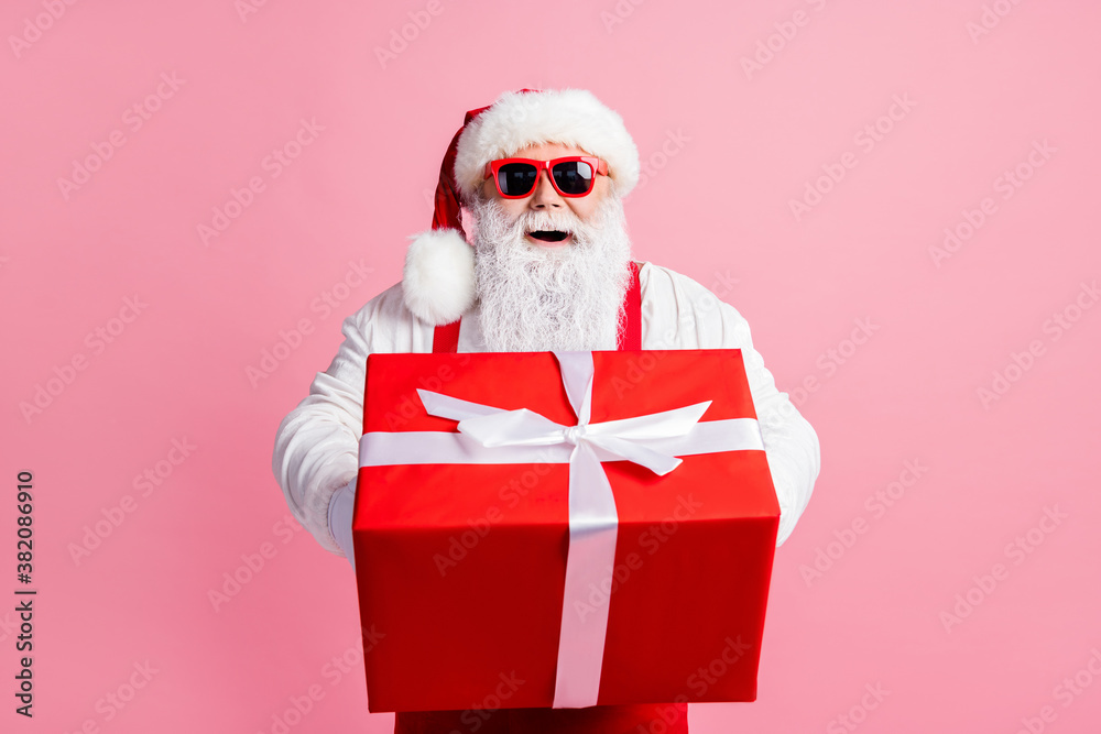 Portrait of his he nice attractive cheerful cheery Santa father holding in hands giving handling large giftbox congratulation congrats greetings North Pole isolated over pink pastel color background - obrazy, fototapety, plakaty 